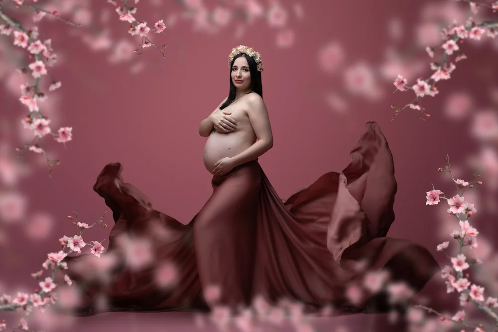 Femme enceinte en robe rose parmi des fleurs de cerisier.