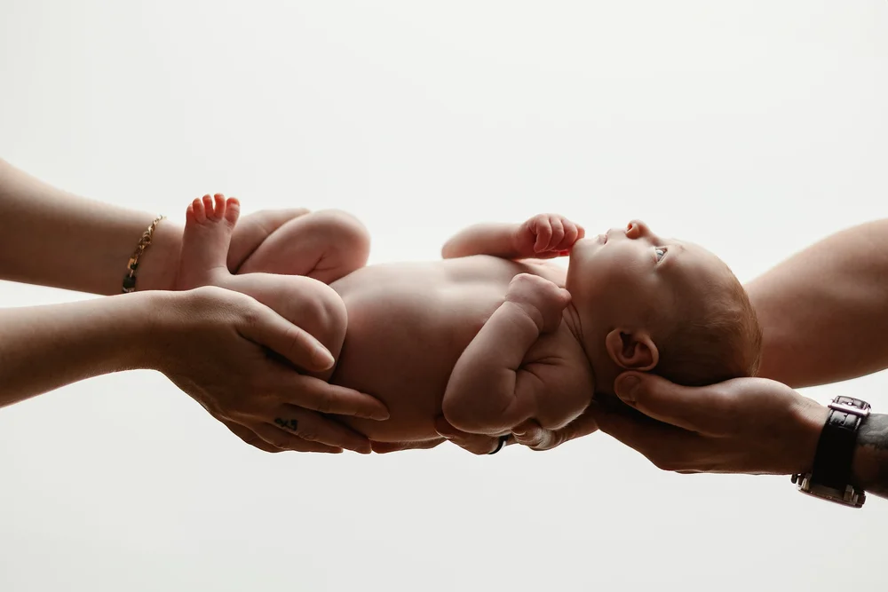Nouveau-né porté dans les mains de ses parents, en contre-jour.