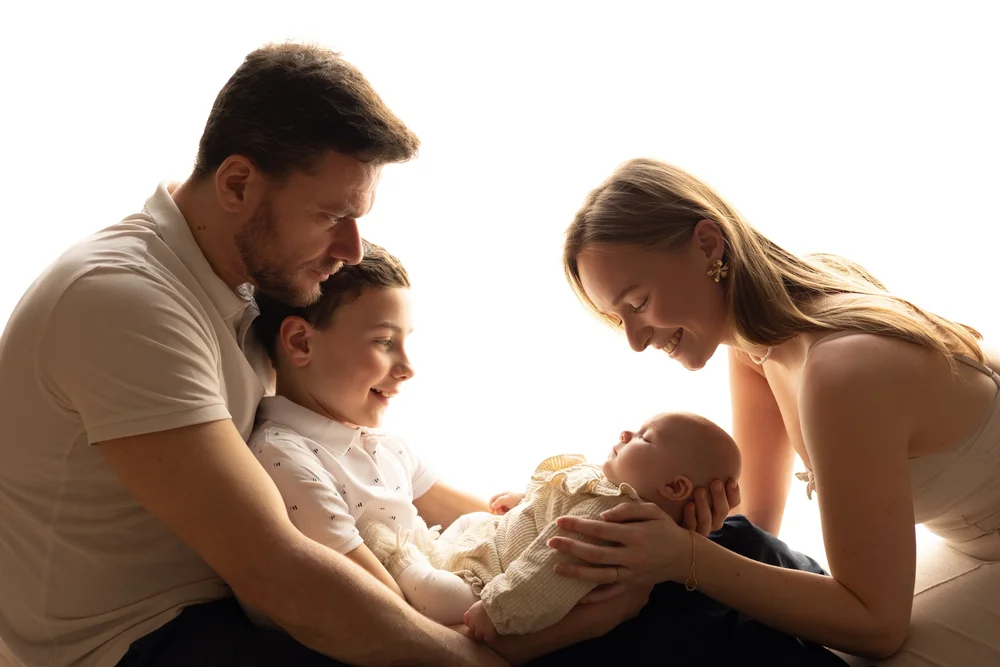 Parents et grand frère autour du nouveau-né, en contre-jour.