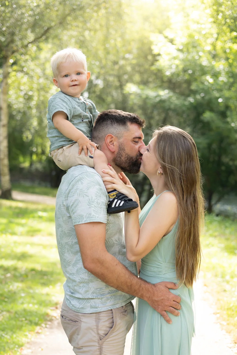 Parents s’embrassant, l’enfant sur les épaules de papa, en extérieur.