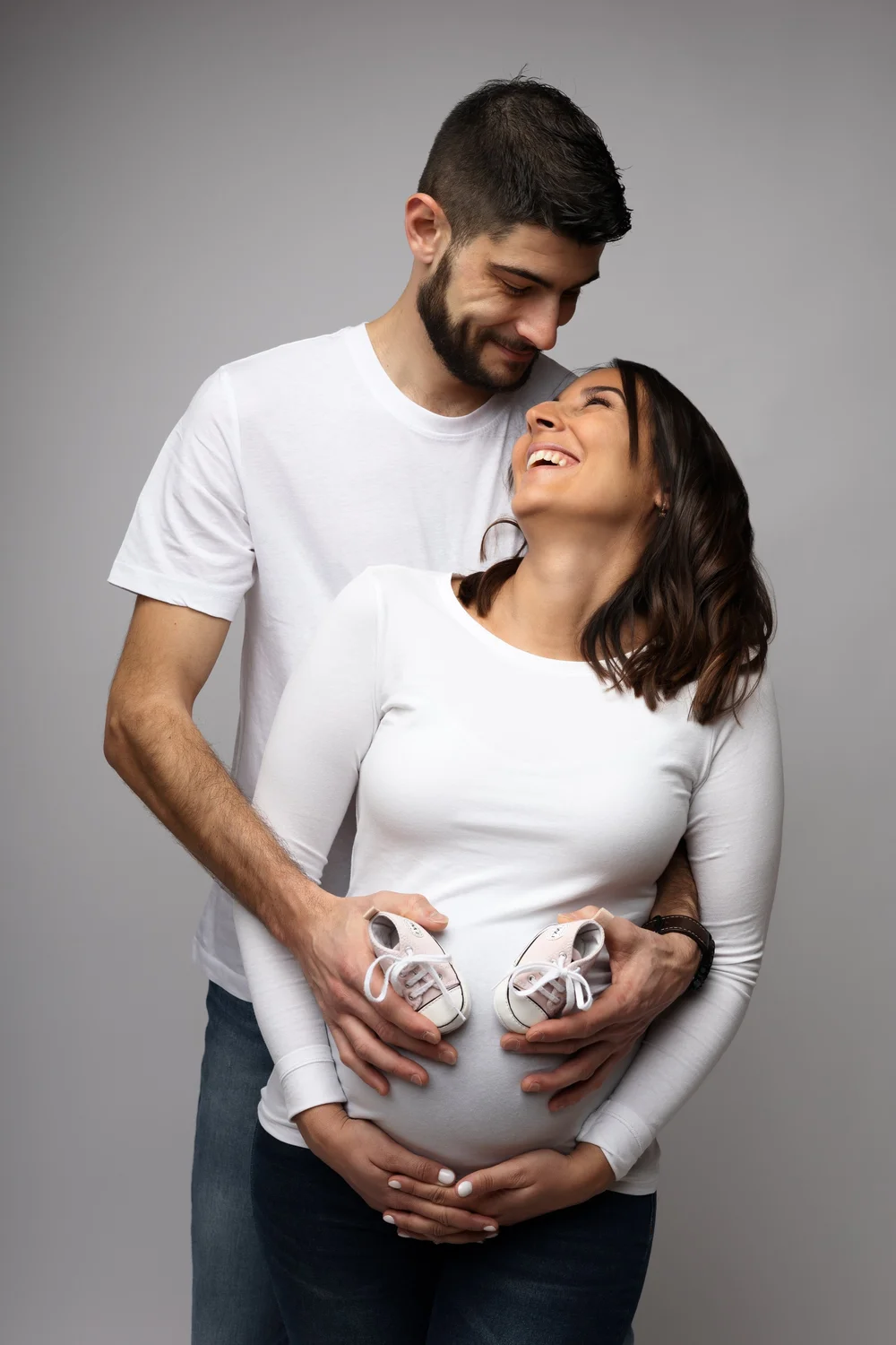 Couple en studio tenant des chaussons de bébé devant le ventre.