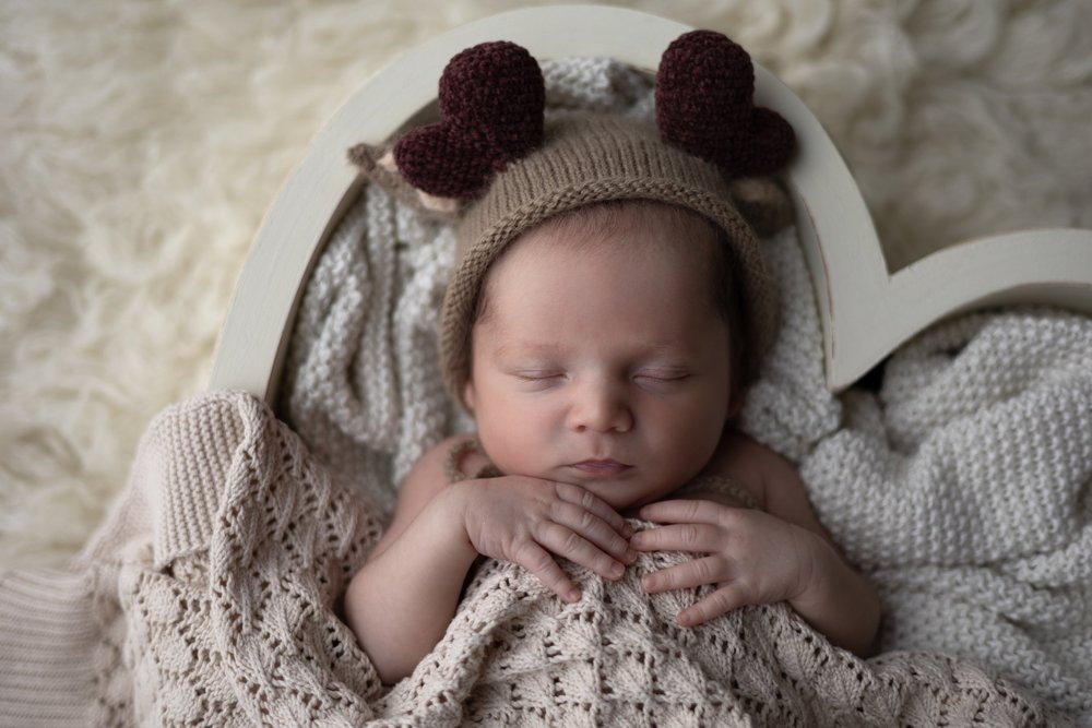 Nouveau-né endormi en bonnet d’ourson dans un panier en cœur.