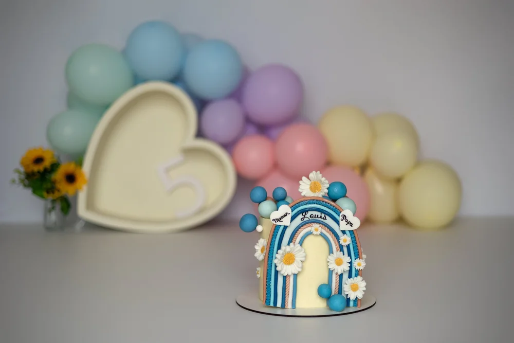 Gâteau arc-en-ciel bleu devant un cœur et des ballons pastel.