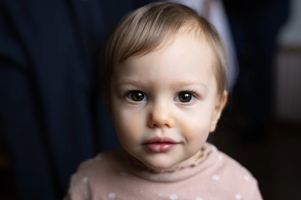 Portrait rapproché d’un bébé en haut rose, sur fond sombre.