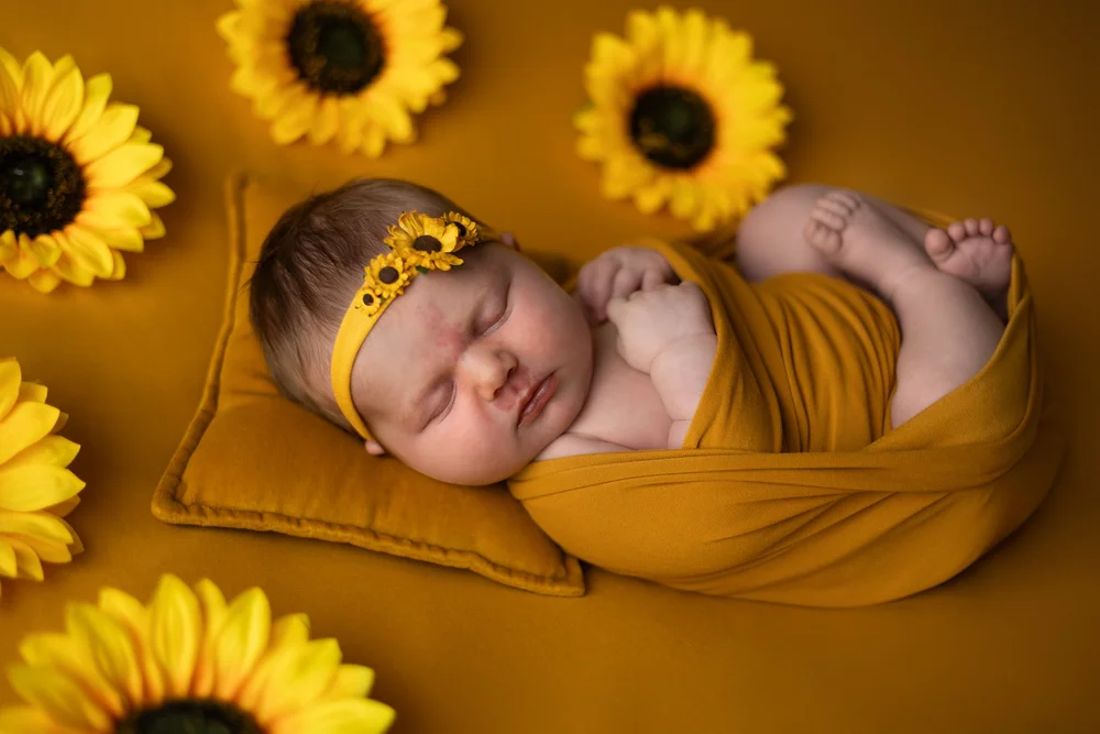 Nouveau-né emmailloté de jaune parmi des tournesols.