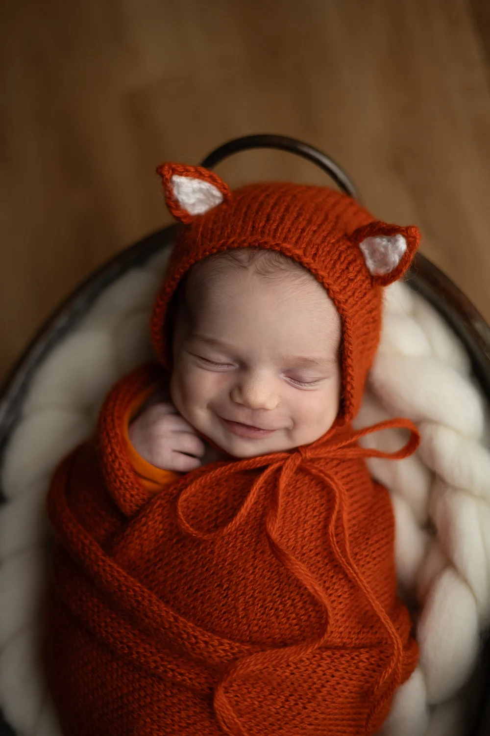 Nouveau-né endormi en bonnet de renard orange.