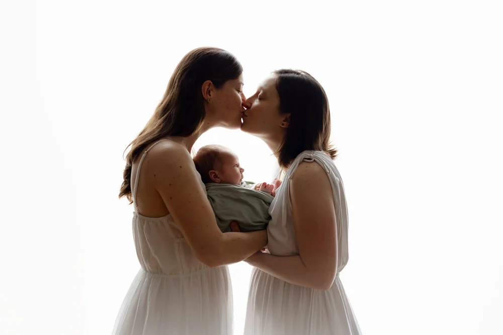 Deux mamans front contre front tenant leur nouveau-né, en contre-jour.
