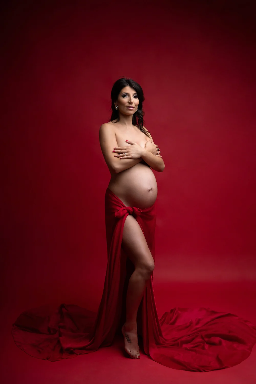 Femme enceinte en robe rouge fendue, sur fond rouge.