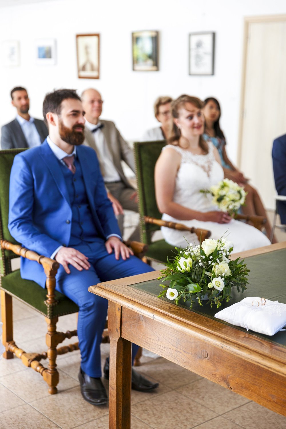 Mariés assis à la mairie, invités derrière eux.