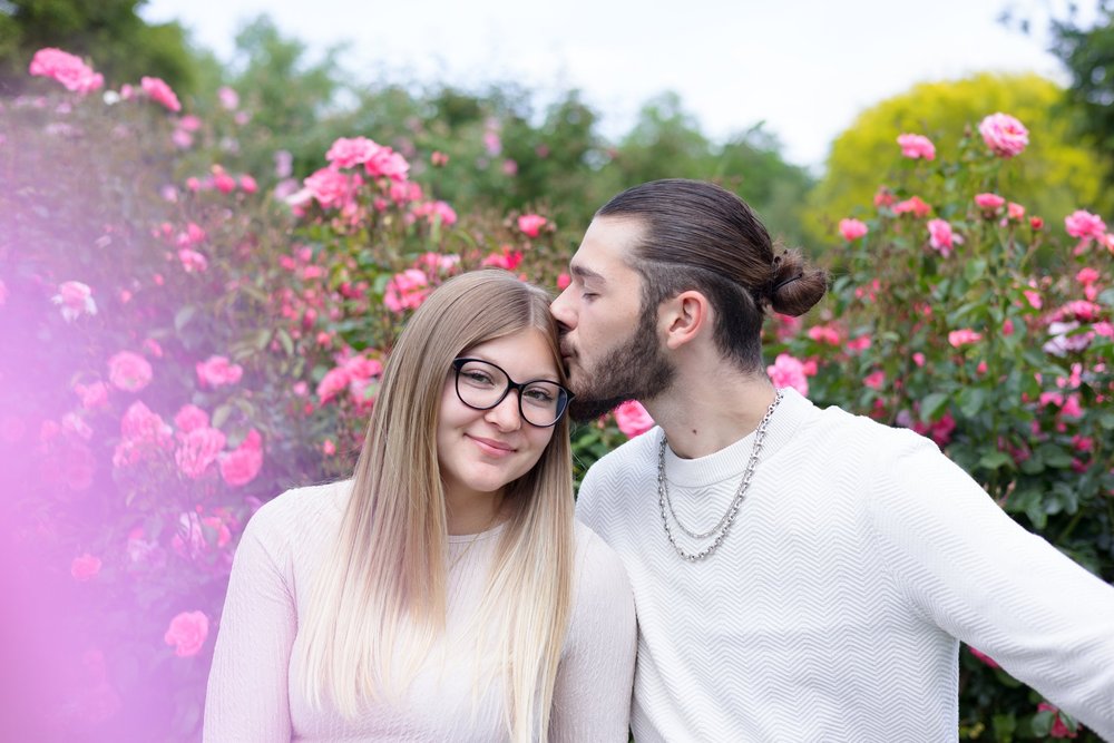 Couple enlacé devant des rosiers roses.