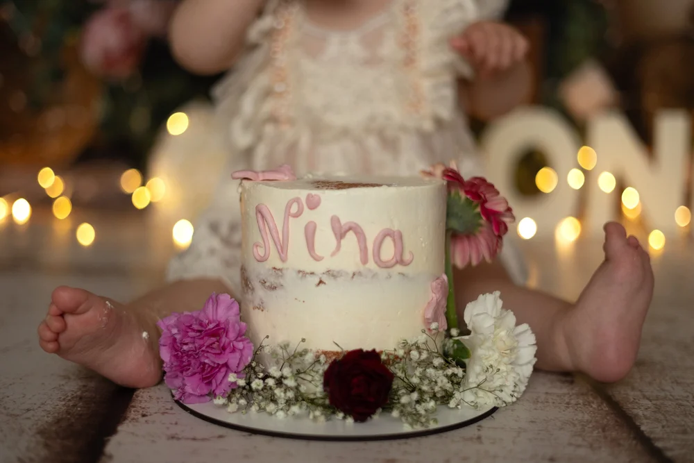 Gâteau d’anniversaire blanc et rose avec des fleurs, pieds de bébé.