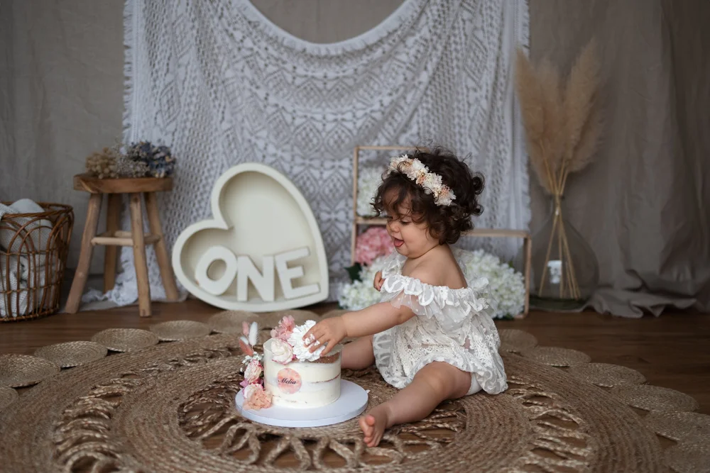 Bébé goûtant son gâteau devant un cœur « ONE », décor bohème.