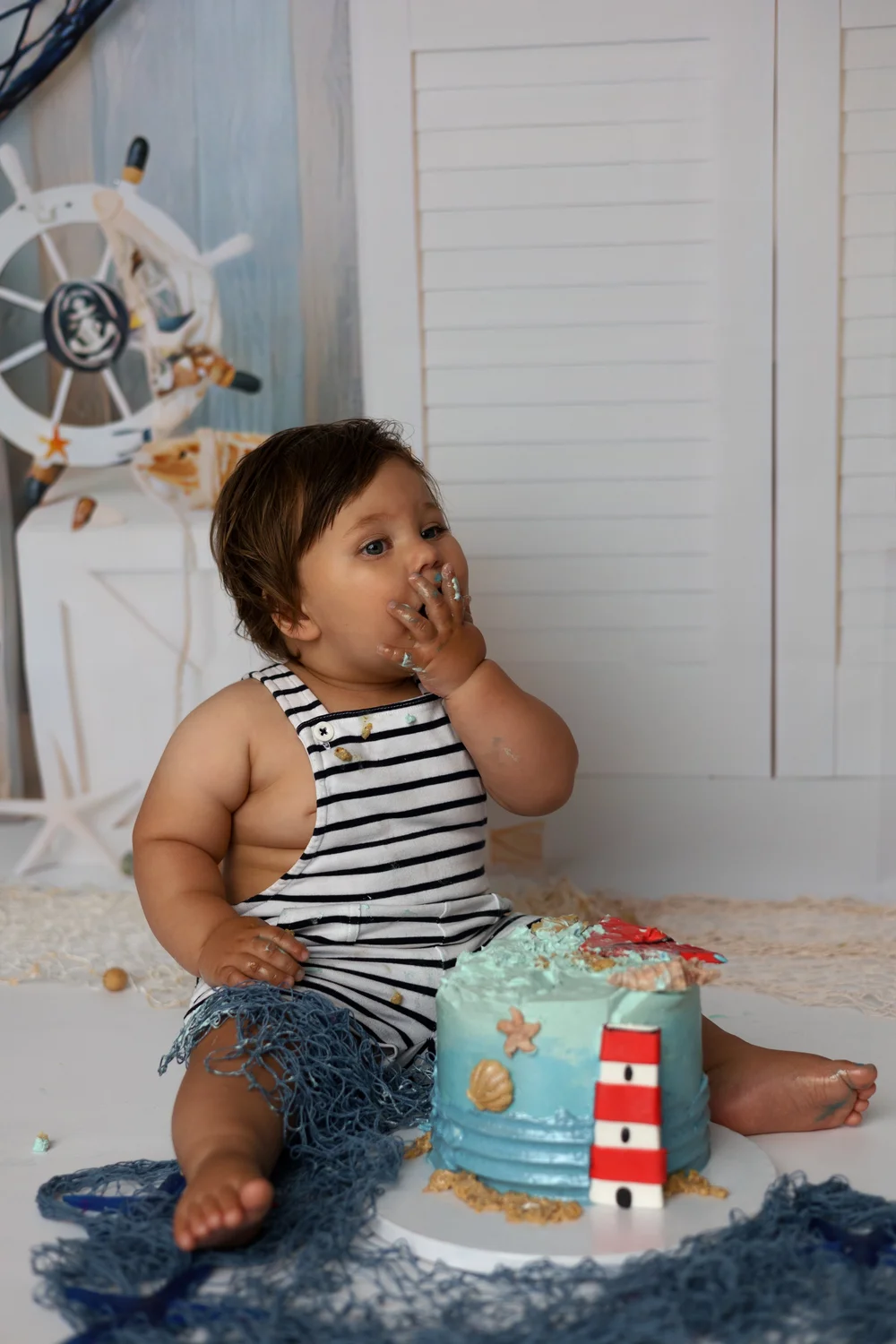 Bébé en marinière goûtant son gâteau phare, décor marin.