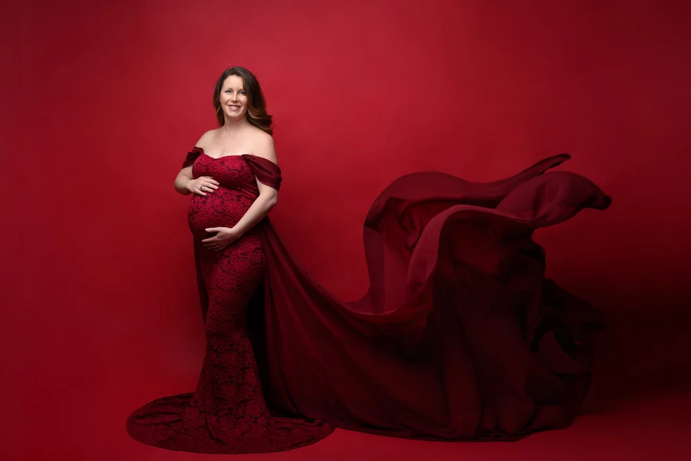 Femme enceinte en robe rouge à traîne, sur fond rouge.