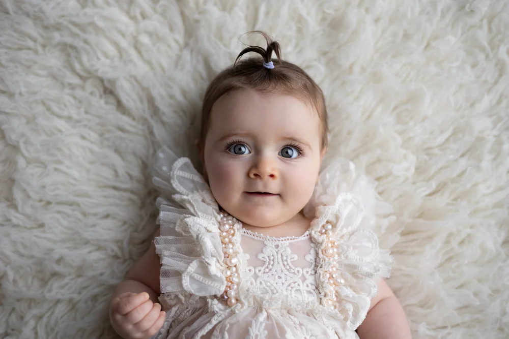 Bébé en robe de dentelle allongée sur une fourrure, vue de dessus.