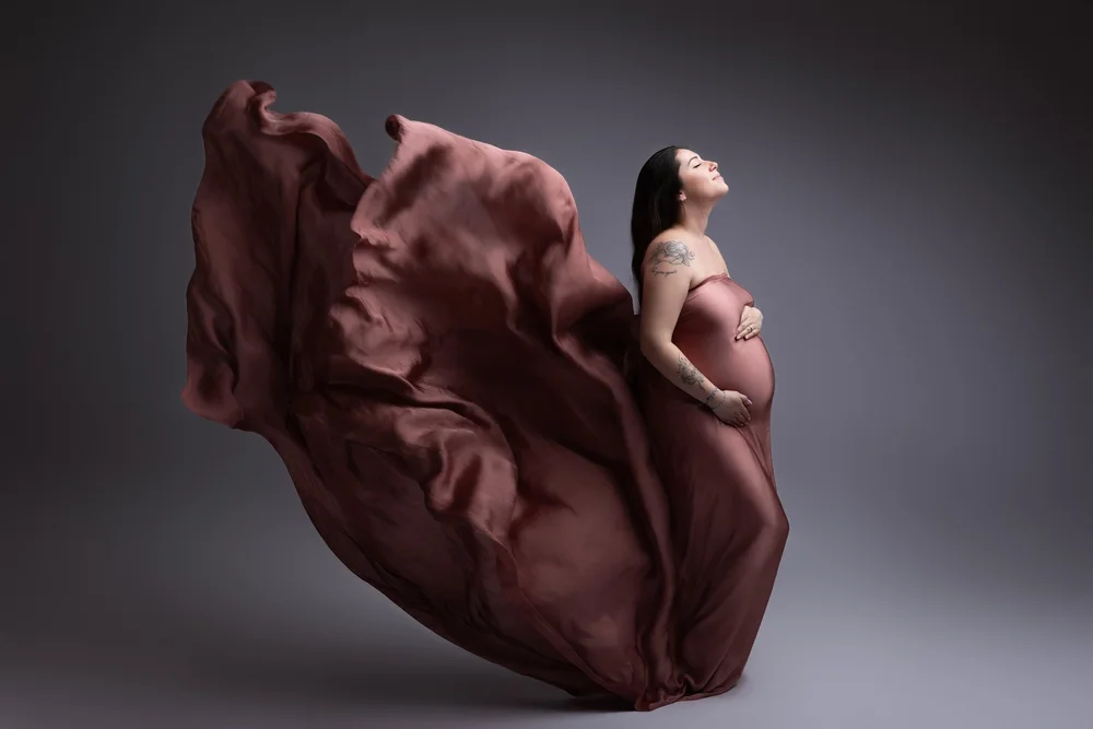 Femme enceinte drapée d’un voile rose qui vole, en studio.