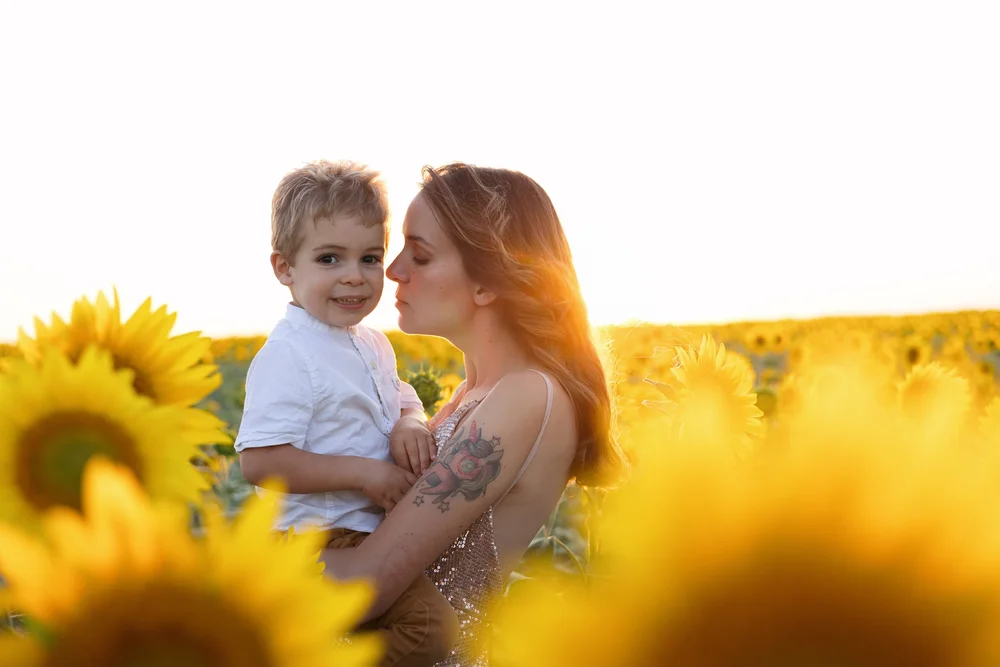Maman embrassant son enfant dans un champ de tournesols au soleil couchant.