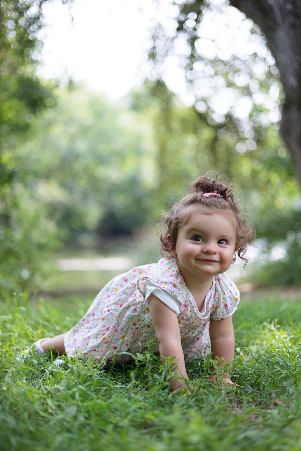 Bébé en robe fleurie à quatre pattes dans l’herbe.