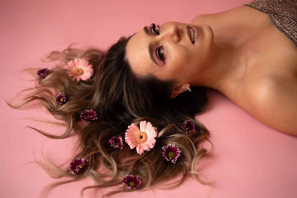 Femme allongée avec des fleurs dans les cheveux, sur fond rose.