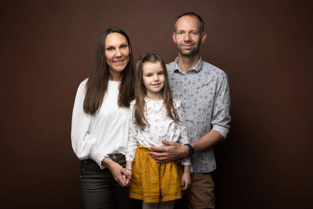 Famille de trois en studio, sur fond brun.