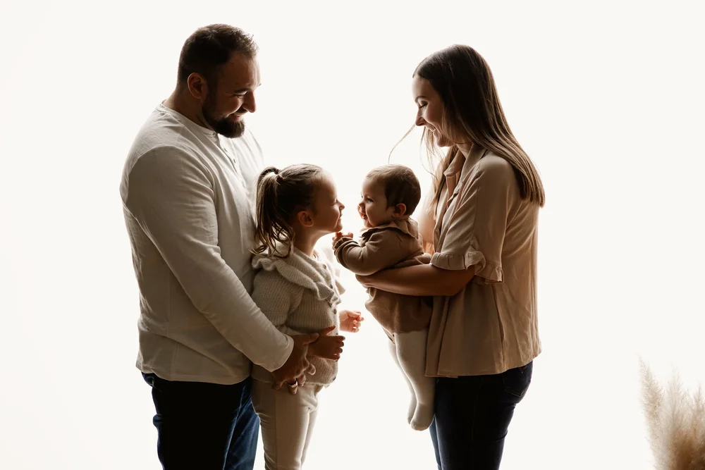 Famille de quatre en contre-jour, les parents portant les enfants.