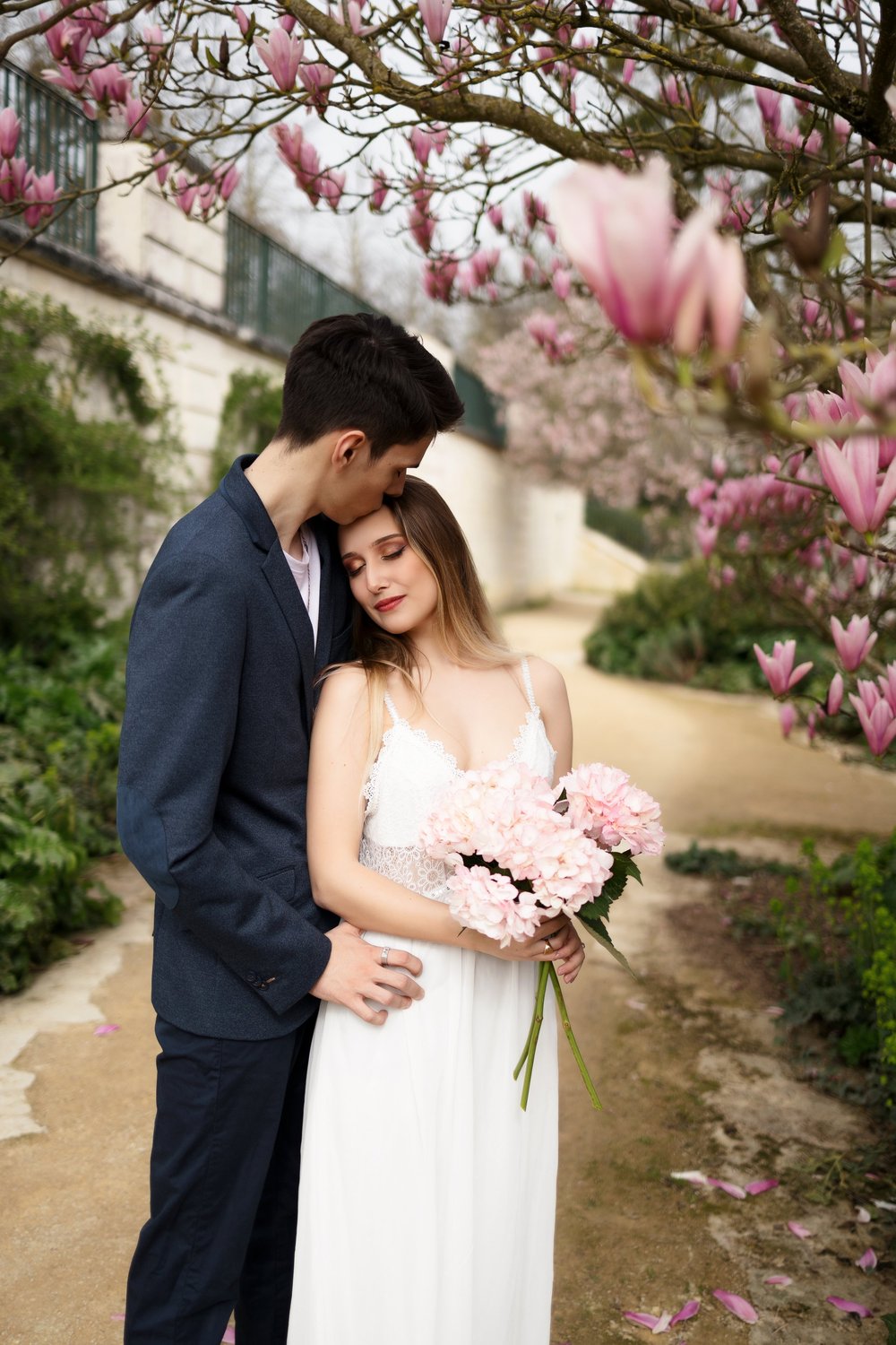 Couple sous un magnolia en fleurs, elle tenant un bouquet.