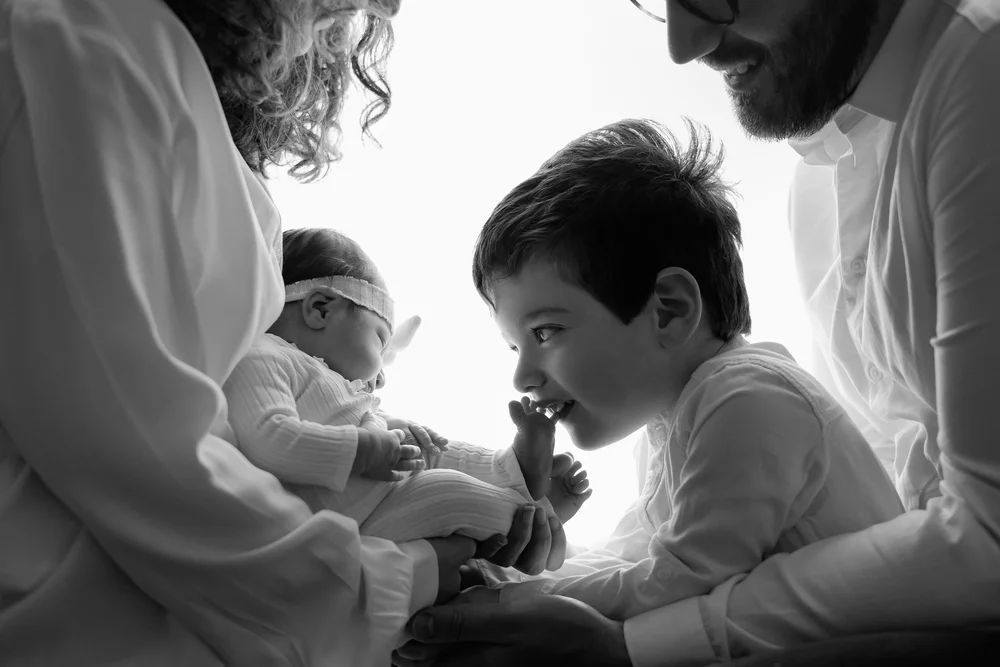 Parents et grand frère autour du nouveau-né, en noir et blanc.