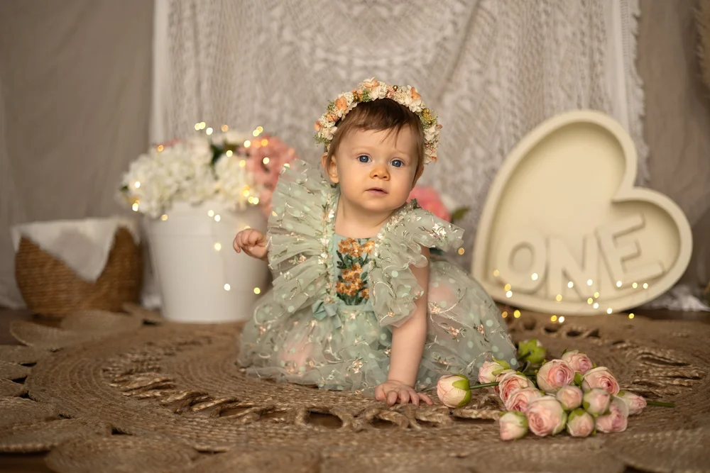 Bébé en robe verte avec un cœur « ONE » et des fleurs.