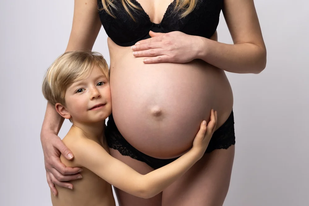 Petit garçon serrant le ventre rond de sa maman.