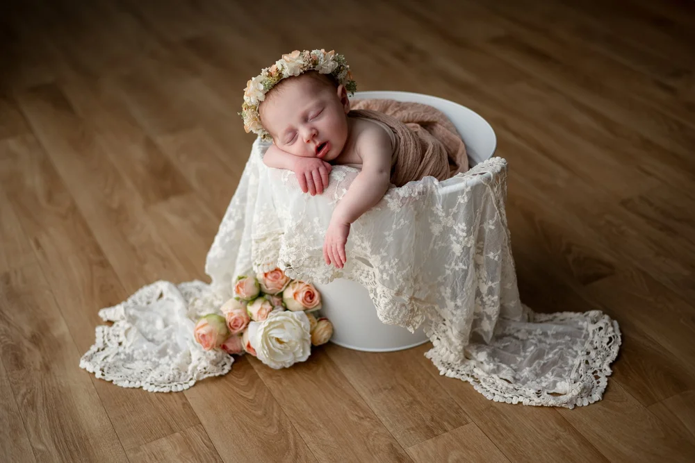 Nouveau-né endormi dans un seau blanc garni de dentelle et de fleurs.