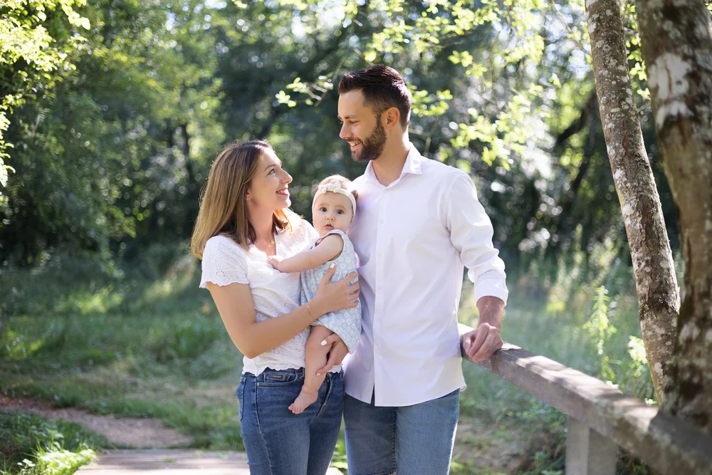 Famille de trois dans un parc, le bébé dans les bras.