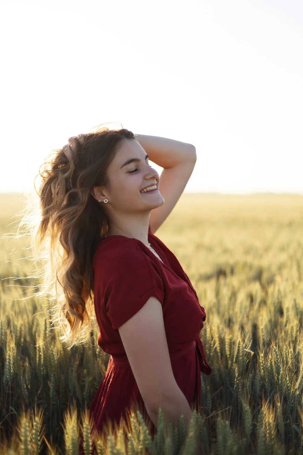 Femme en robe rouge riant dans un champ de blé au soleil.