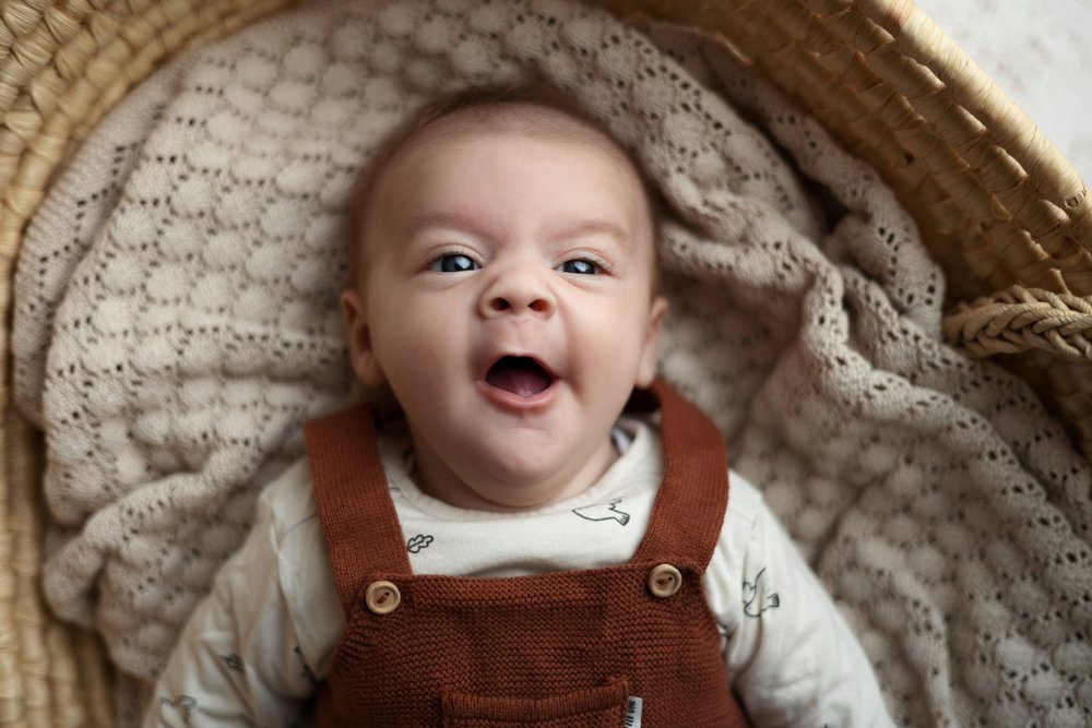 Bébé souriant en salopette rouille dans un panier.