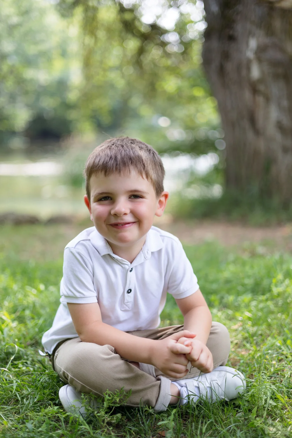 Petit garçon assis en tailleur dans l’herbe, devant un lac.