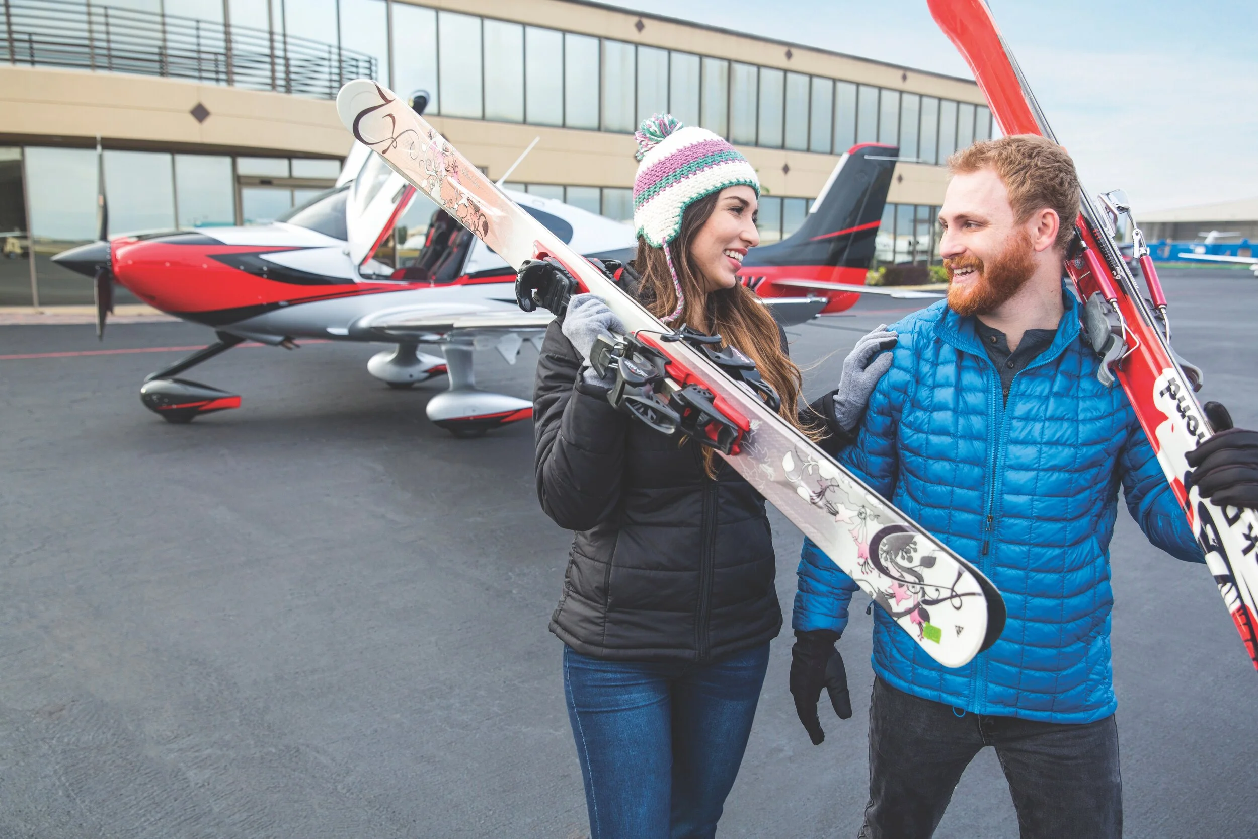 Woman and man holding skis in front of a private plane