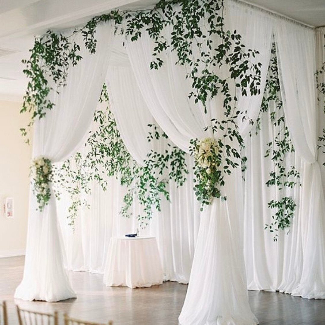 White chuppah with white draping and greenery.