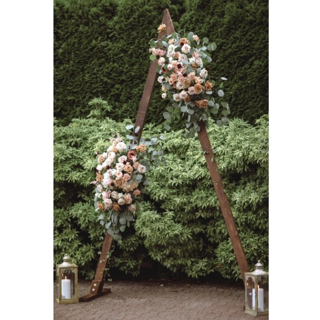 Rustic wooden triangle wedding arch with flowers.