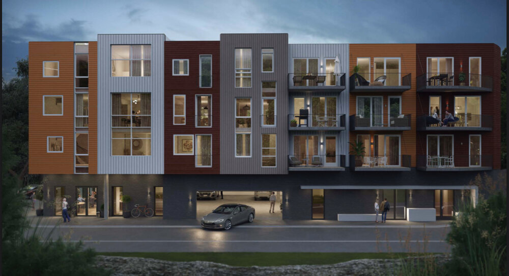 Moderne leilighetsbygning om kvelden med flere etasjer, store vinduer og balkonger. Det er parkerte biler og mennesker utenfor bygningen.