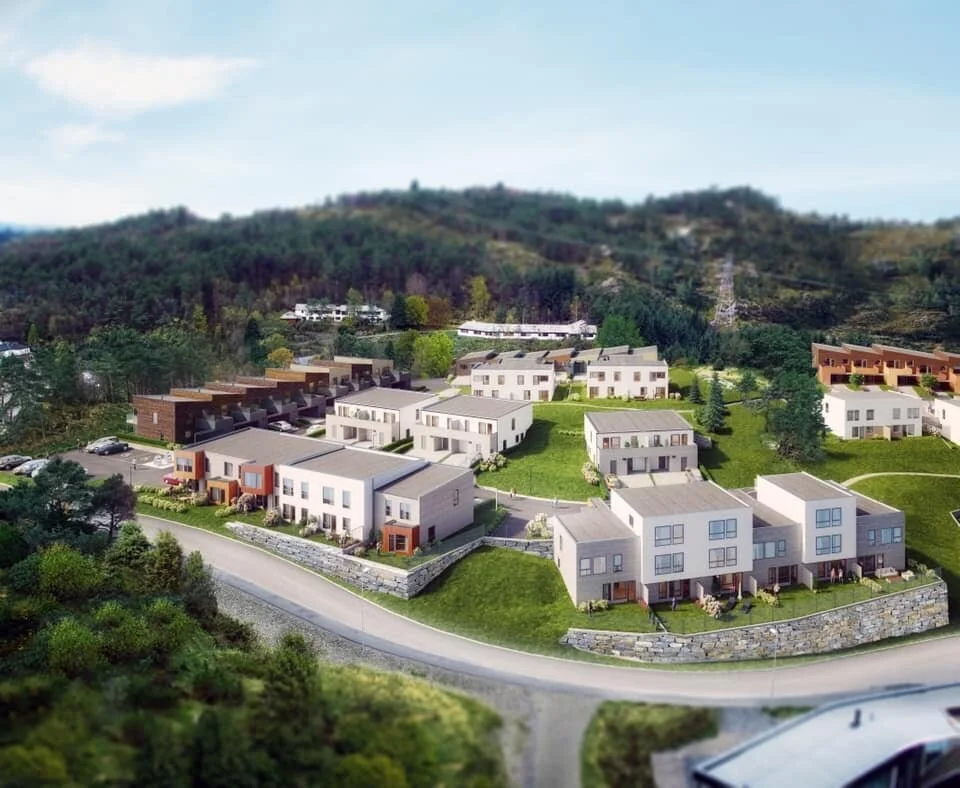 Nytt boligområde med moderne rekkehus og tomannsboliger omgitt av naturgrønt landskap og trær, med åser i bakgrunnen.