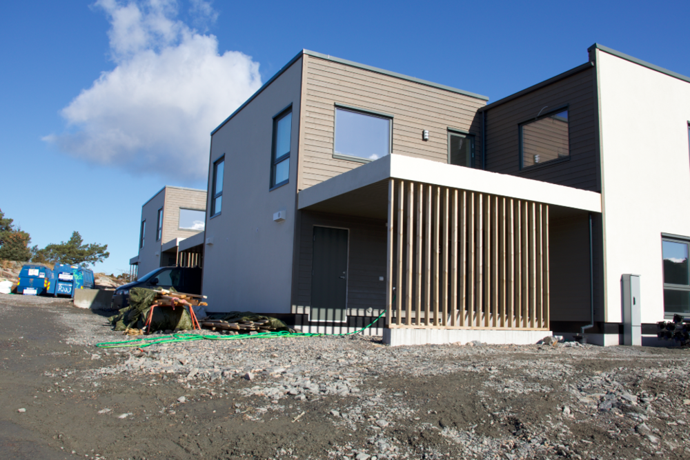 Moderne bolig under byggeprosess med grus i forgrunnen, omgitt av blå himmel og skyer.