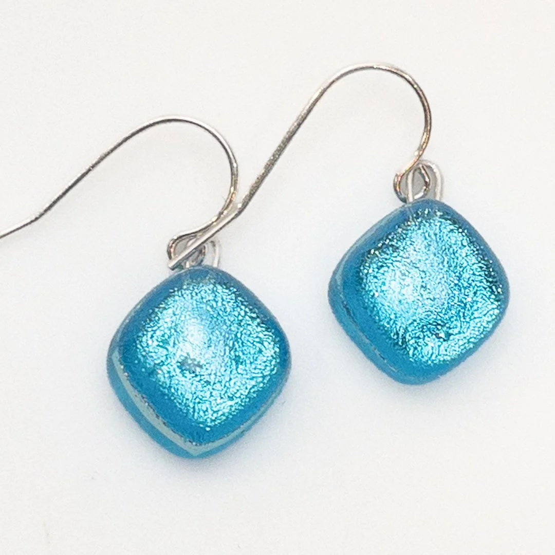 A pair of handcrafted Splash! fused dichroic glass earrings in vibrant ocean blue, set on sterling silver hooks.