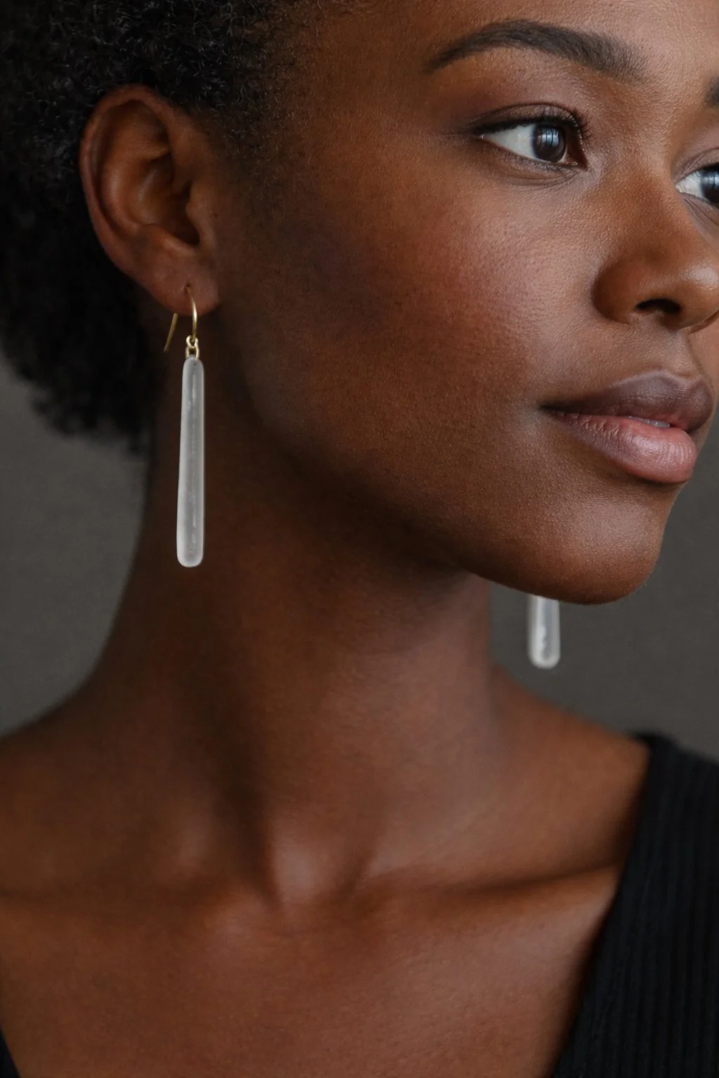 Black woman wearing long pearlescent fused dichroic glass earrings handmade on Vinalhaven Island, Maine.