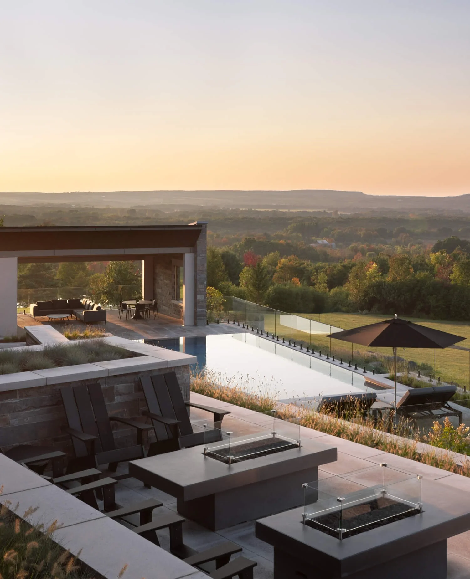 Luxury modern house with outdoor living area, swimming pool, and scenic view of rolling hills and trees at sunset.