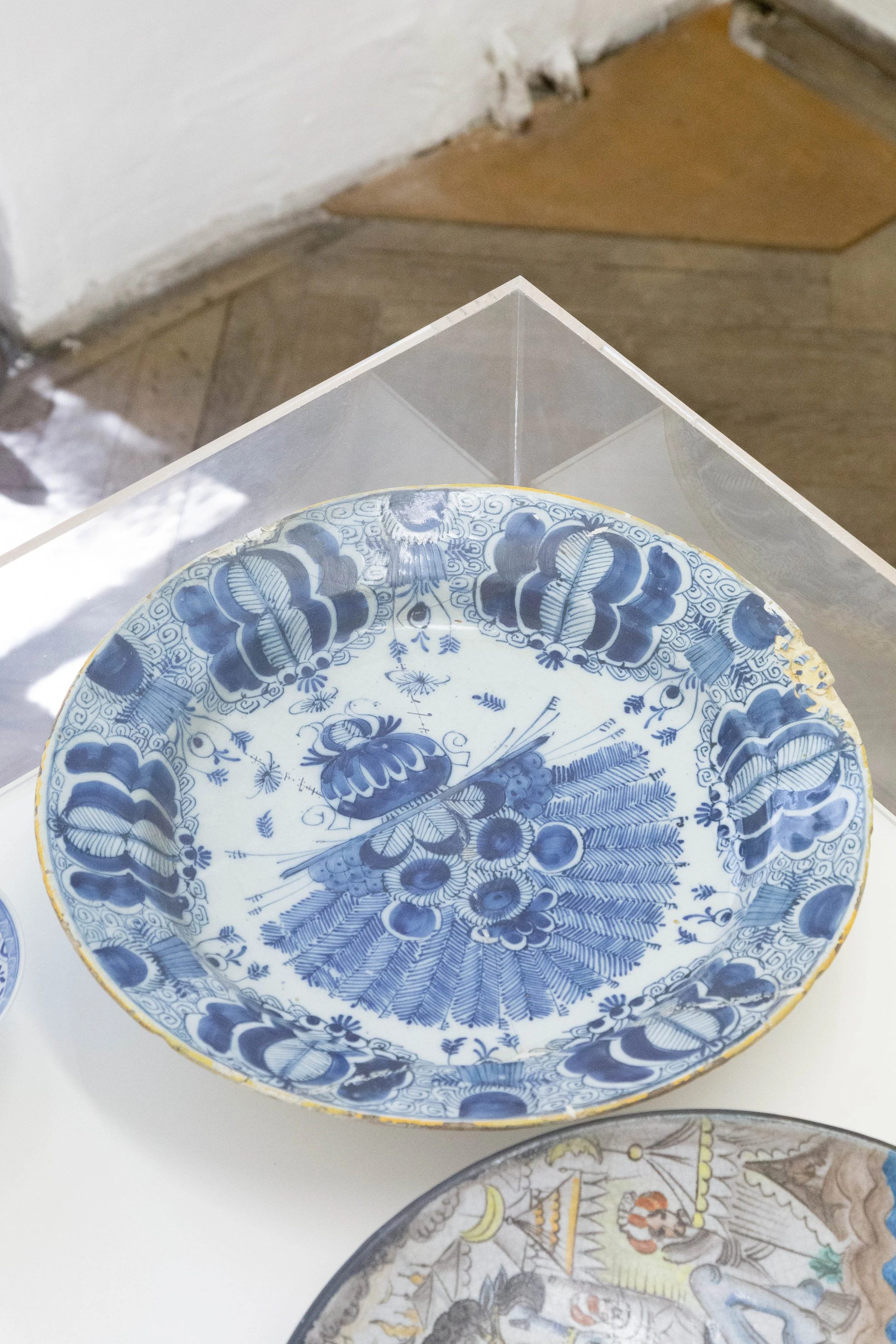   fig39   le monde , 2026, plywood, cardboard, acrylic glass, 86,5 x 125 x 50 cm, Plate with tulip and peacock pattern  De Klauw , Delft, Netherlands, probably late 18th century, Faience, broken and glued, heavily chipped, Ø 35,5 cm, ht. 6,7 cm, Acqu