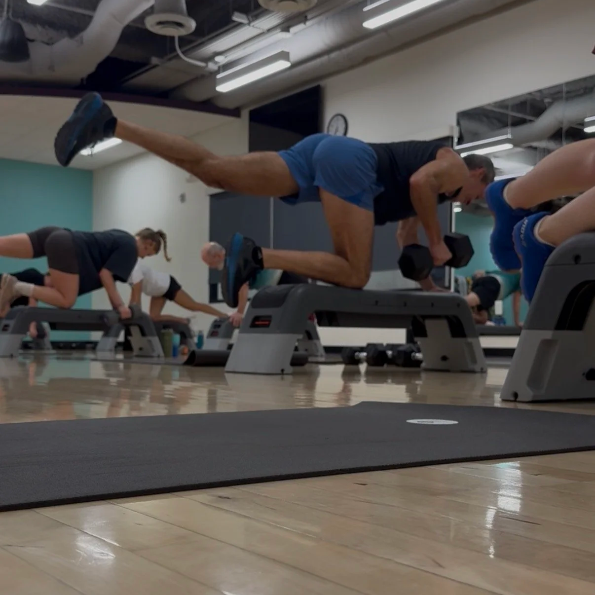 A group of people perform a bird dog row exercise while kneeling off workout benches