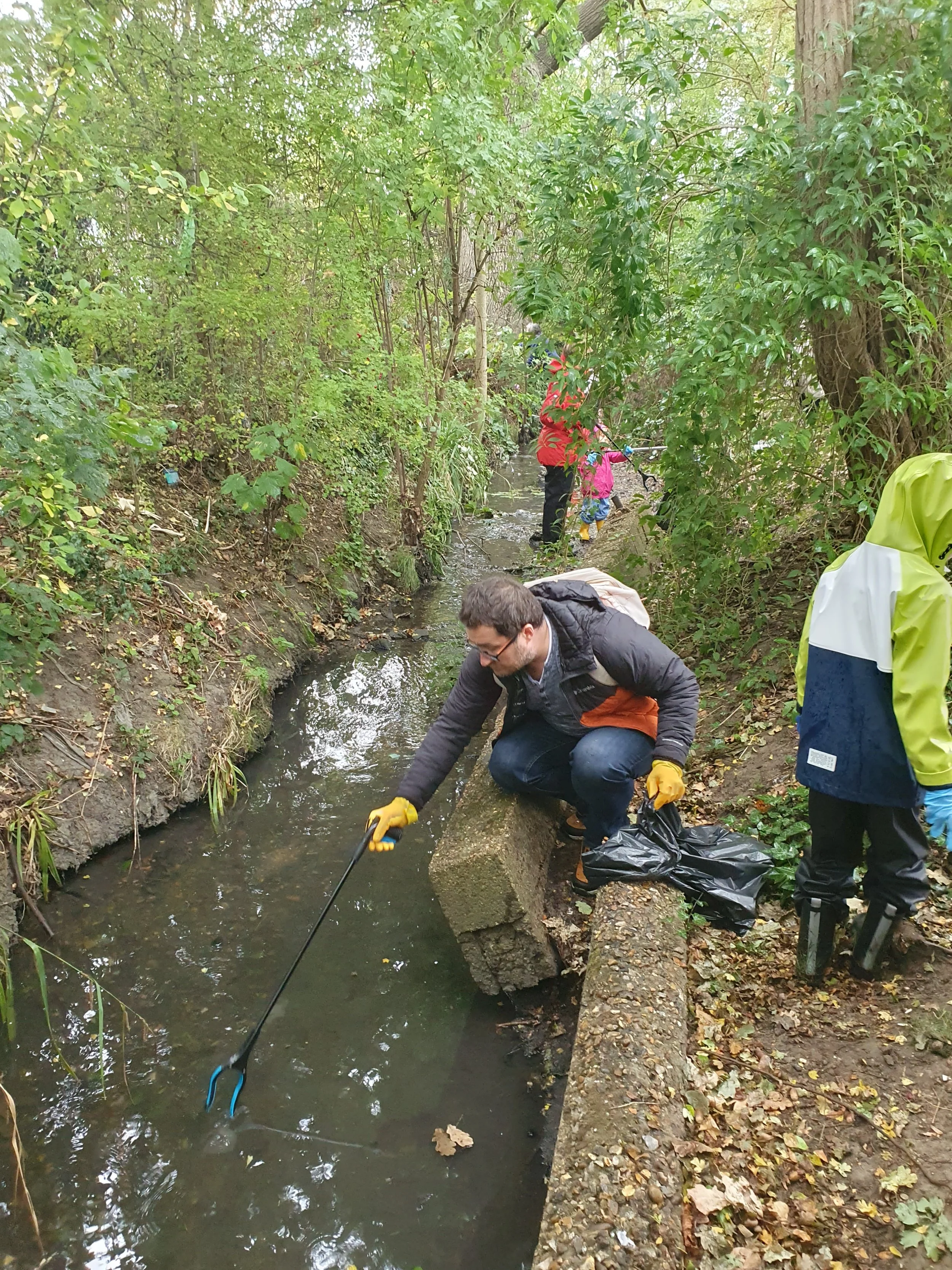 People cleaning a creek surrounded by trees, using tools and trash bags
