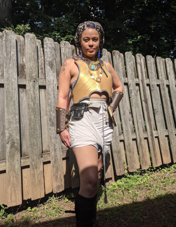 Image of Kira in LARP costume, gold breastplate, jewelry, and bracers. 