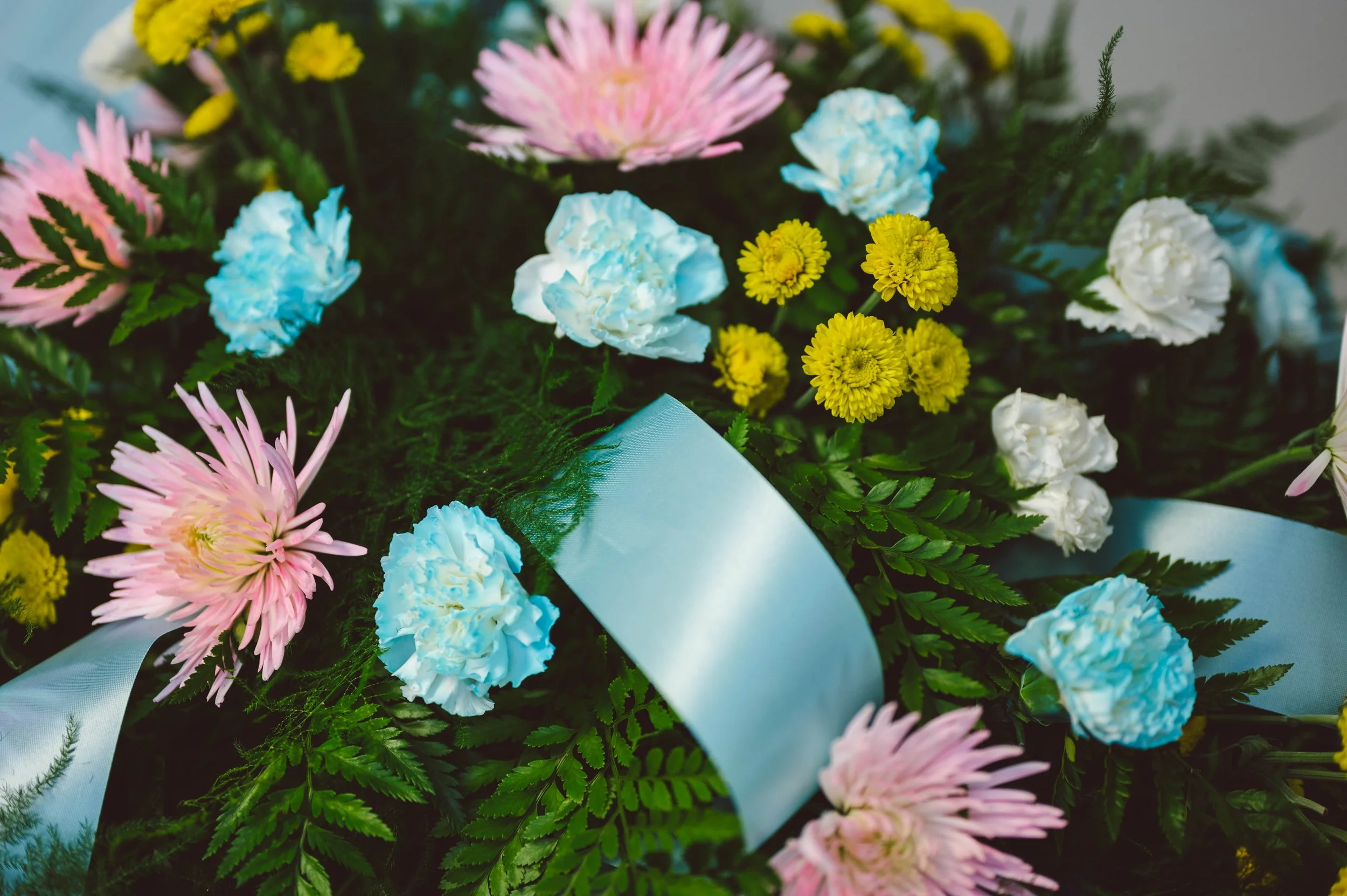 A colorful bouquet of pink, blue, white, and yellow flowers with green foliage and a light blue ribbon.
