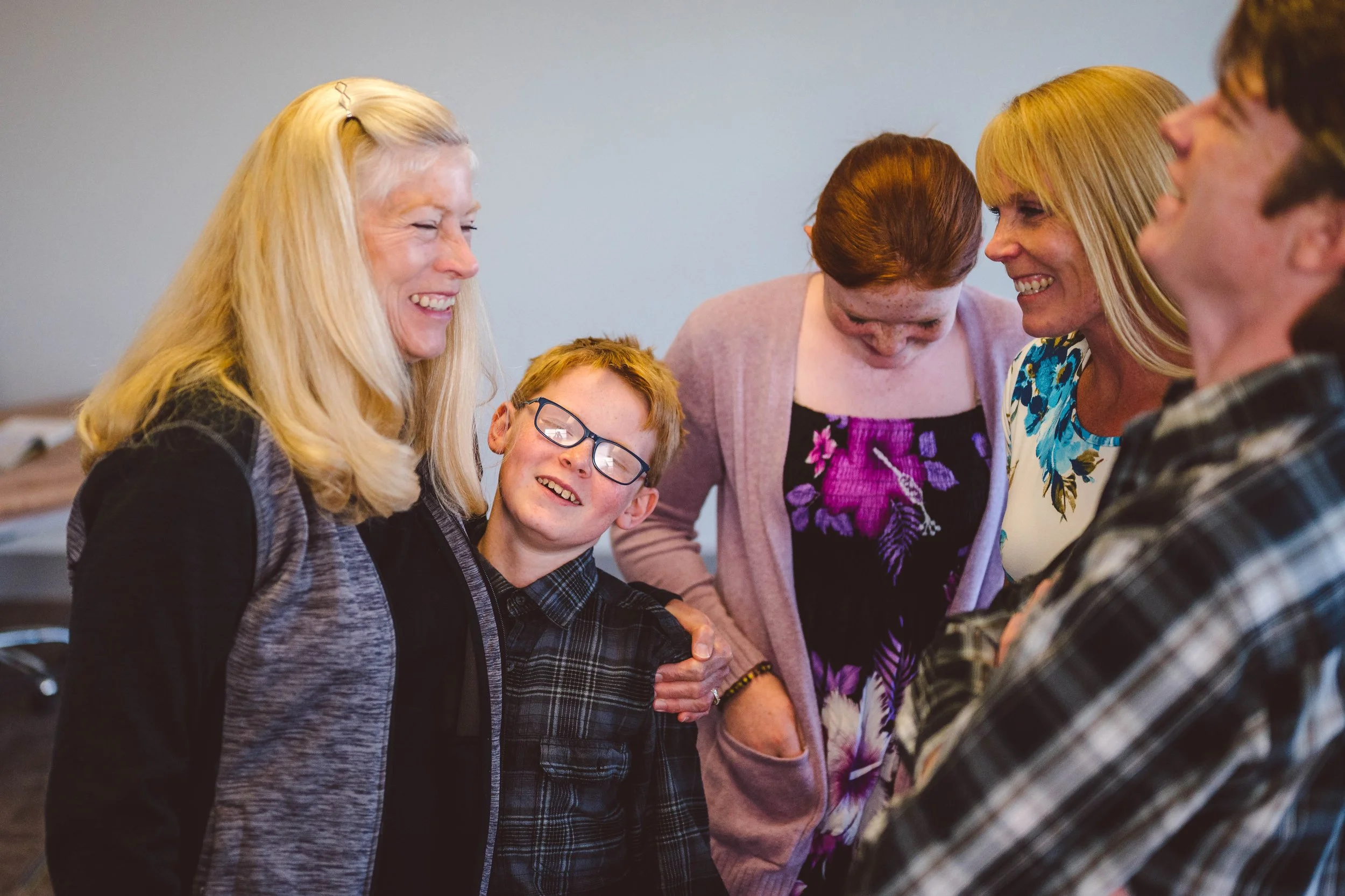 A group of five people, including three women and two males, smiling, hugging, and engaging in a joyful moment.