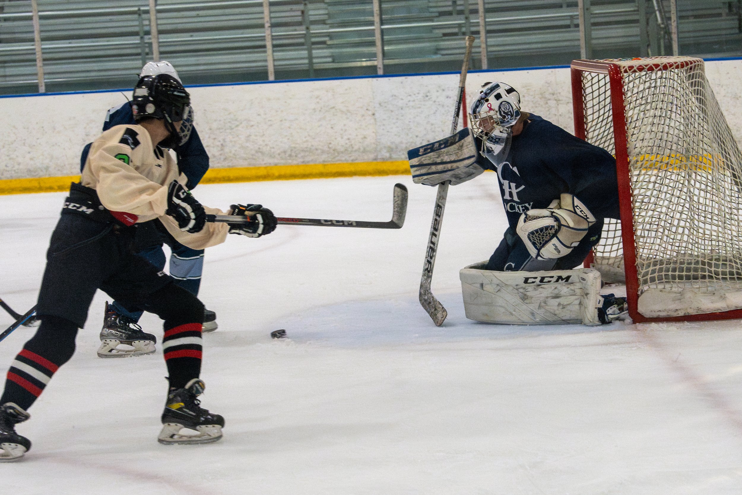 Ice hockey game with a player shooting the puck towards the goal as the goalie prepares to block it.